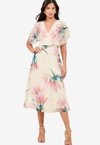 Vestido midi con estampado floral en crema, con flores rosas y verdes, que presenta un escote en V profundo, mangas cortas y una cintura ajustada.