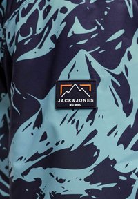 Tessuto di giacca blu e navy con motivi astratti. Presenta un'etichetta nera con il logo "JACK&JONES" e accenti grafici di montagna.