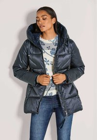 Marineblauwe gewatteerde jas met een grote capuchon, ritssluiting en zijzakken; heeft een quilted ontwerp en een glanzende, soepele textuur.