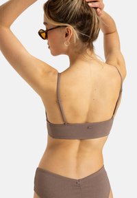 Top bikini marrone con texture, dotato di sottili spalline regolabili e un logo decorativo. Il modello è di spalle, evidenziando il design posteriore.