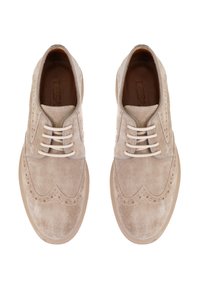 Chaussures en suède beige à lacets avec un design à bout ailé, des détails perforés et une semelle en caoutchouc beige clair. Les lacets sont de couleur crème.