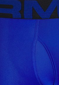 Shorts de sport bleus avec une taille élastique noire portant du texte. Le tissu est lisse avec un léger éclat et un design épuré.