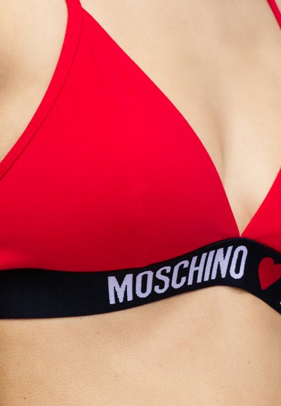 Κόκκινο μπικίνι τοπ τρίγωνο με μαύρο ελαστικό λουράκι που έχει λευκό κείμενο "MOSCHINO" και κόκκινη καρδιά στο σώμα ενός ατόμου.