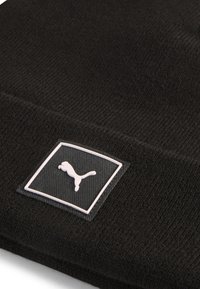 Gorro de punto negro con un acabado texturizado y un logotipo rectangular blanco que presenta un puma estilizado. Diseño simple y versátil.
