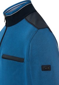 Giacca blu con chiusura a zip e texture a costine, con dettagli neri sulle spalle e una tasca rifinita con bordo nero a contrasto. Collo con risvolto e dettaglio a righe.