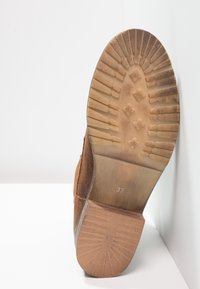 Hnědé semišové kotníkové boty s texturovanou gumovou podrážkou, která se vyznačuje květinovým vzorem pro trakci a velikostním označením "37" na spodní straně.