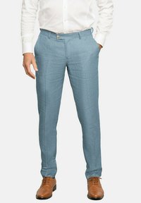 Pantalones de lino de color azul claro con un acabado texturizado, que cuentan con una cinturilla con pasadores y un cierre de un solo botón. Combinados con zapatos de cuero marrón.