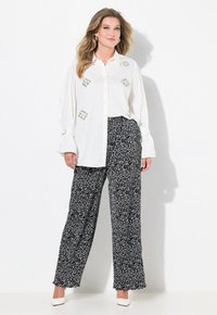 Biała koszula z guzikami, ozdobiona haftami, w połączeniu z szerokimi spodniami w czarno-biały wzór, dopełniona białymi szpilkami.