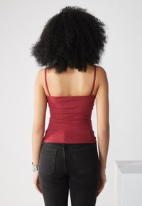 Burgunderfarget ribbet tanktop med tynne stropper, tettsittende design som fremhever midjen, kombinert med svarte høytaljede jeans.