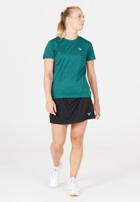 Teal sports t-shirt lavet af glat stof, parret med en sort nederdel. Viser logoer på begge stykker, med en tætsiddende design til aktivt brug.