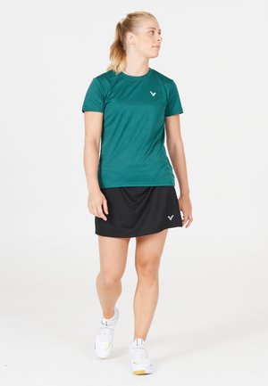 Teal sports t-shirt lavet af glat stof, parret med en sort nederdel. Viser logoer på begge stykker, med en tætsiddende design til aktivt brug.