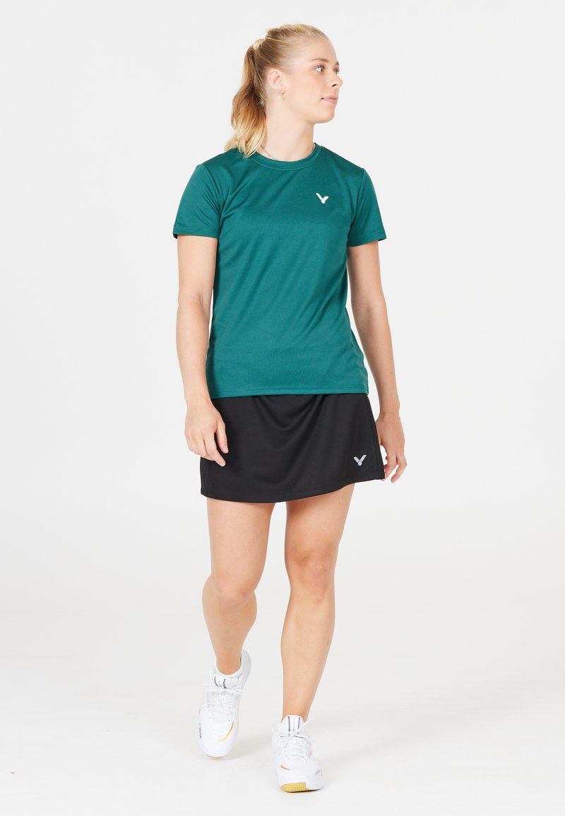 Teal sports t-shirt lavet af glat stof, parret med en sort nederdel. Viser logoer på begge stykker, med en tætsiddende design til aktivt brug.