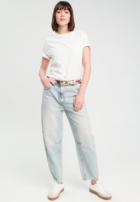 Hvid bomulds t-shirt, lyseblå højtsiddende jeans med afslappet pasform, mønstret bælte og hvide sneakers med tan såler.