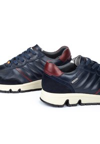 Baskets en cuir bleu marine avec des accents bordeaux, en suédine texturée, dotées de coutures apparentes et d'une semelle en caoutchouc blanc avec un motif de crantage.