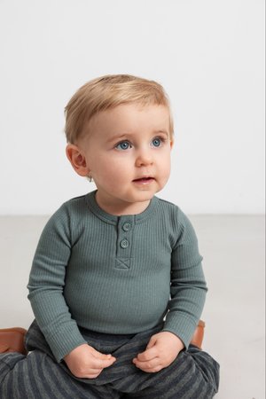 Langermet, ribbet, teal skjorte med tre knapper og et lite merke, kombinert med mørke stripete bukser. Barn som sitter på gulvet.