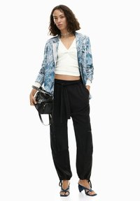 Blazer con motivo a pattern blu e bianco, top bianco aderente, pantaloni neri con coulisse e sandali blu con tacco. Accessori includono una borsa nera e una collana girocollo argento.