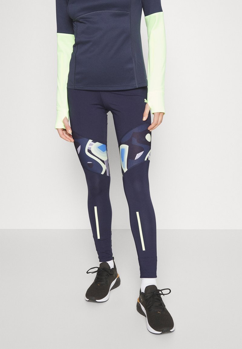 Leggings de sport navy avec des motifs abstraits en bleu et blanc, présentant des accents réfléchissants et une coupe ajustée. Assortis avec un top noir et des chaussures.