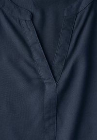 Tessuto blu navy con una superficie liscia presenta una scollatura a V e dettagli di cucitura sottili lungo i bordi, creando un design pulito.