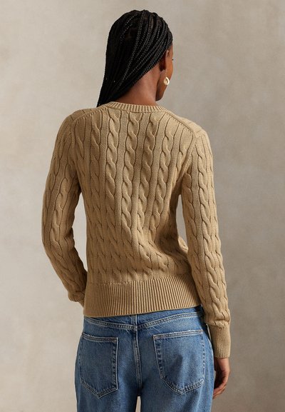 Džemper od pletenine u bež boji s uzorkom kabela, rebrastim manžetama i rubom, uparен s svijetloplavim trapericama visokog struka, prikazan s leđa.