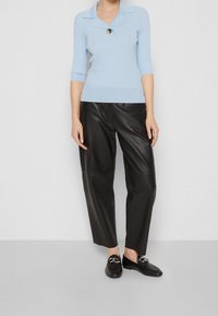 Jasnoniebieski prążkowany sweter z szpiczastym kołnierzem i czarnym guzikiem, zestawiony z wysokim stanem czarnych skórzanych spodni i czarnych mokasynów.