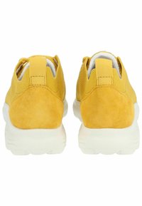 Gelbe Sportschuhe mit einem strukturierten Wildleder-Obermaterial und Mesh-Einsätzen, ausgestattet mit einer weißen gepolsterten Sohle und Fersenlaschen für ein einfaches Anziehen.
