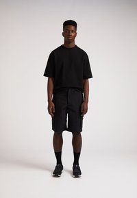 Schwarzes T-Shirt mit kurzen Ärmeln kombiniert mit schwarzen Cargo-Shorts. Getragen mit schwarzen Socken und schwarzen Turnschuhen. Glattes Material mit lässiger Passform.