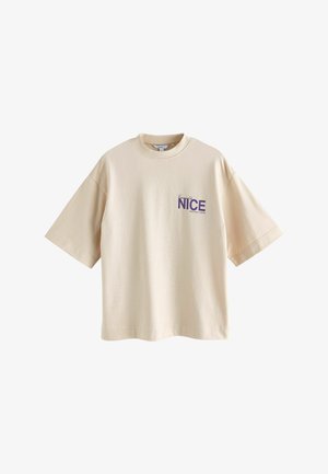 T-shirt en coton beige à coupe oversize, manches courtes, col rond, avec le texte violet "NICE Edition 2020" sur la poitrine gauche.