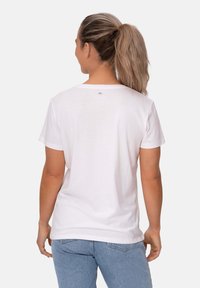 Camiseta de algodón blanca de corte relajado, con mangas cortas, escote redondeado y un detalle mínimo en la etiqueta en la parte posterior. Combinada con unos vaqueros azul claro.
