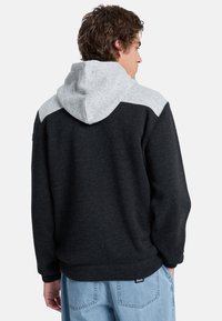 Felpa grigia scura con cappuccio strutturato grigio chiaro e pannelli sulle spalle. Presenta una tasca a marsupio e polsini a costine, realizzata in un tessuto morbido.