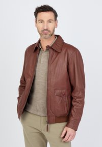 Braune Lederjacke mit Reißverschluss, Knopfklappen-Tasche und gerippten Bündchen. Kombiniert mit einem grauen Polo-Shirt und beigen Hosen.