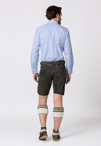 Camicia a maniche lunghe blu a scacchi con bottoni, pantaloni corti in pelle nera, scaldamuscoli bianchi lavorati a maglia e scarpe marroni con suola texturizzata.
