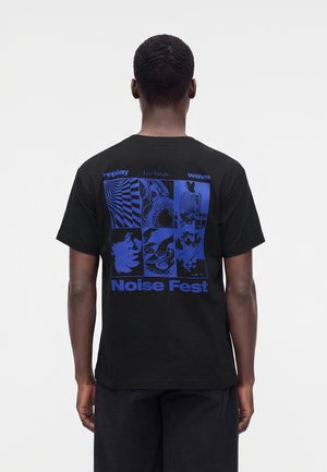 Person von hinten gesehen, trägt ein schwarzes T-Shirt mit blauen grafischen Flächen und Text "Noise Fest," "replay," "Live Tonight...," und "wave."
