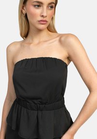 Haut noir sans bretelles en tissu doux avec un ourlet peplum froncé, présentant des détails froncés au niveau du décolleté et une taille élastique pour un ajustement parfait.