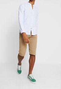 Chemise à rayures bleu clair avec boutons, short kaki et baskets vertes. Tenue décontractée avec une coupe droite et des manches courtes.