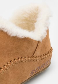 Botte en daim marron avec doublure en fausse fourrure, détails cousus et semelle en caoutchouc. Le côté affiche le nom de la marque en relief "SOREL."