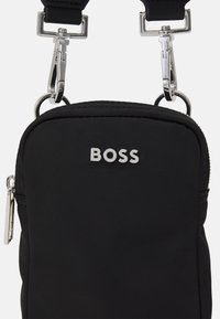 Borsa crossbody compatta nera con logo "BOSS" in argento e ganci metallici sulla tracolla regolabile, chiusura a zip laterale.