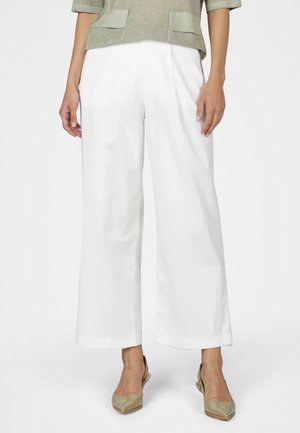 Frau trägt weiße, weite, verkürzte Hose, beige Slingback-Pumps mit spitz zulaufender Spitze und ein strukturiertes hellgrünes Oberteil mit kurzen Ärmeln.