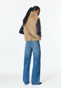 Bézs műszőrme mellény magas gallérral, egy hosszúujjú fekete felső fölött viselve. Széles szárú kék farmernadrág, amelyen szegecselt hátsó zsebek találhatók.