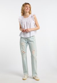 Blusa bianca senza maniche con spalle arricciate, abbinata a jeans strappati di un blu chiaro e sneakers crema. Design semplice, texture morbida, look casual.