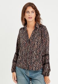 Chemise noire avec un motif floral en nuances de rouge et de crème, manches longues, fermeture à boutons, et accents en dentelle au niveau des poignets.