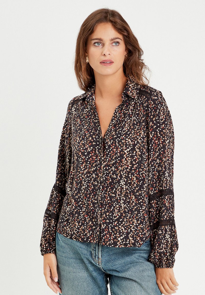 Chemise noire avec un motif floral en nuances de rouge et de crème, manches longues, fermeture à boutons, et accents en dentelle au niveau des poignets.