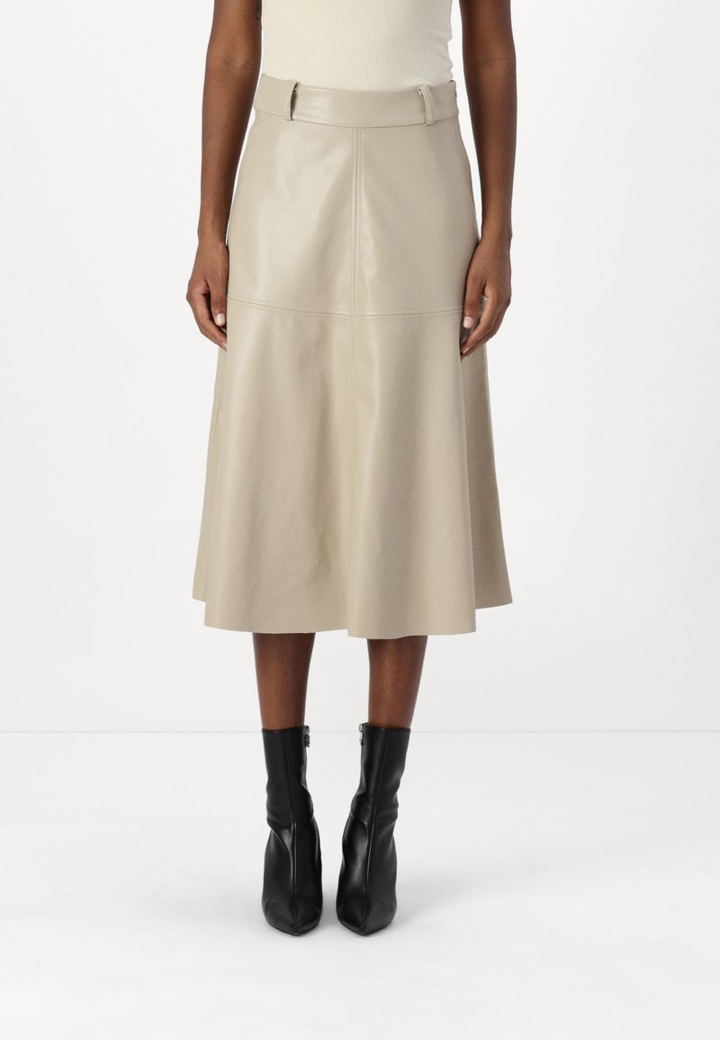 Beige Leder-Midirock mit ausgestellter Form, Reißverschluss und Gürtel in der Taille. Kombiniert mit schwarzen Knöchelstiefeln. Glatte Textur.