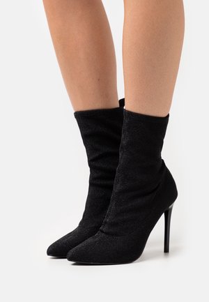 Bottines noires décontractées à cheville avec un bout pointu, un talon aiguilles haut et un tissu texturé avec un léger éclat.