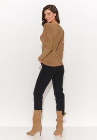 Brązowa bluzka z długim rękawem i bufkami na ramionach, w połączeniu z ciemnymi, obcisłymi dżinsami oraz jasnobrązowymi, wysokimi butami na obcasie. Gładka tekstura materiału.