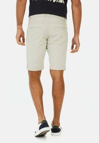 Lichtbeige shorts met twee achterzakken, vlakke voorkant en lengte boven de knie. Gepaard met witte sneakers met marineblauwe accenten.