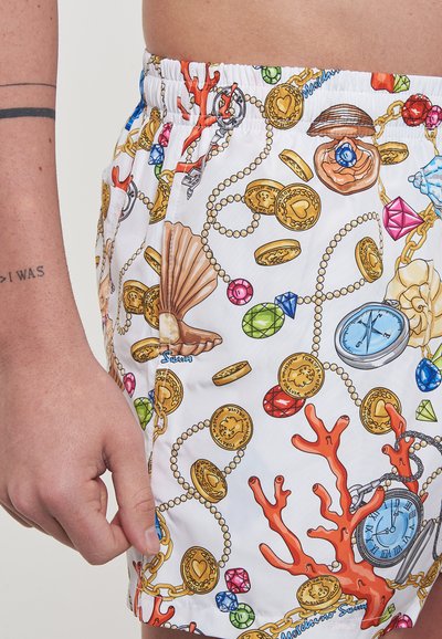 Pantaloni da bagno bianchi con un motivo colorato di conchiglie, corallo, monete, gemme e un orologio. Visibile una cintura elastica e una tasca laterale.
