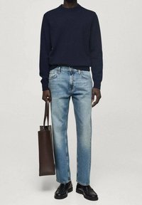 Suéter de punto azul marino, jeans rectos de color azul claro, zapatos de cuero negros y un bolso marrón con diseño minimalista y líneas limpias.