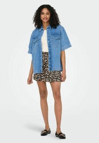 Denim shirt in lichtblauw met korte mouwen en twee voorkeurszakken, gecombineerd met een minirok in luipaardprint en zwarte flats.