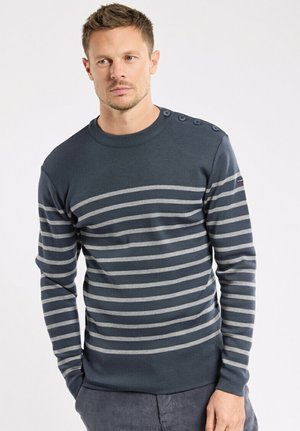 Navyblauwe trui met horizontale grijze strepen, geribbelde ronde hals en decoratieve knopen op de schouder. Zachte gebreide textuur.