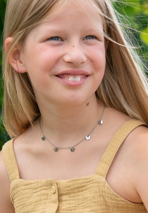 Zilveren ketting met vlinderbedels in groen en zilver, gedragen door een kind, tegen een vervaagde natuurlijke achtergrond.